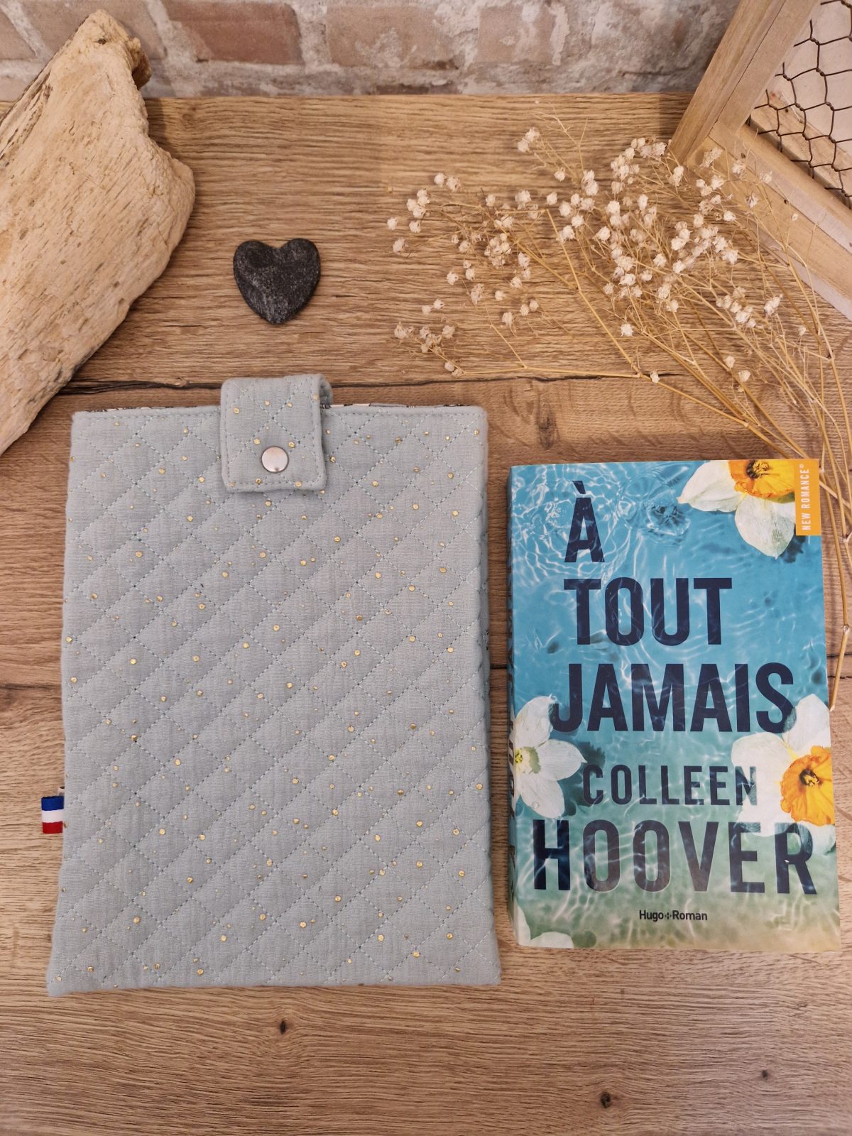 Cette pochette molletonnée avec des tissus uni est un accessoire utile pour ranger votre livre du moment. Tout en coton et molletonnée pour une protection optimale, elle convient au format livre broché classique. Ferme avec un bouton de pression.